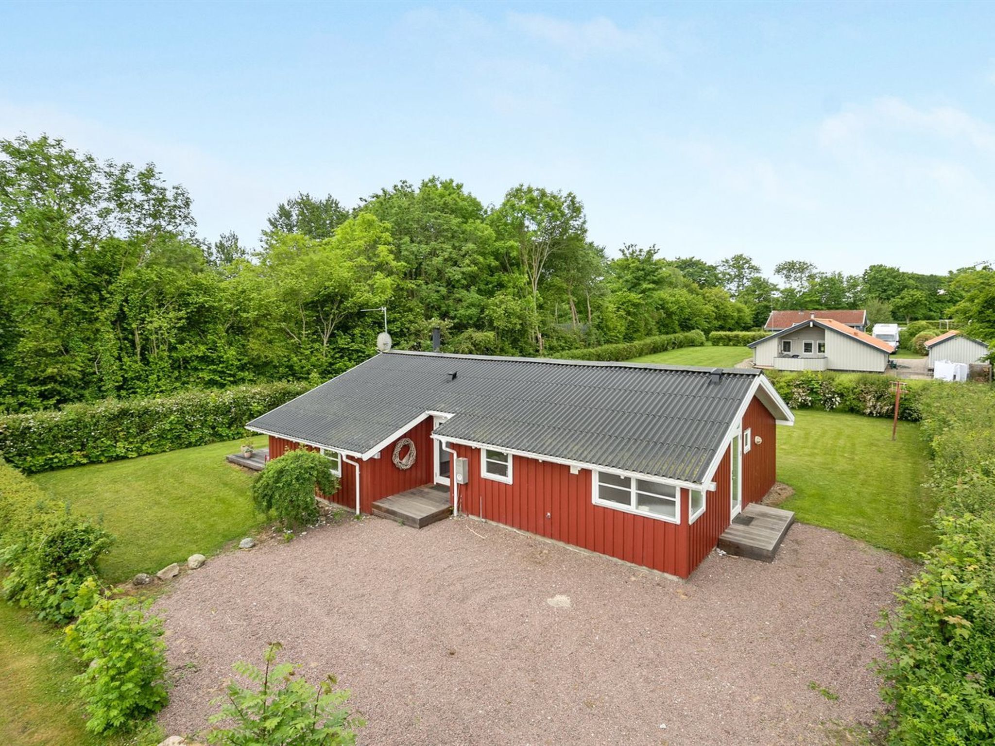 En röd byggnad med en grusuppfart, omgiven av frodig grönska och andra hus.