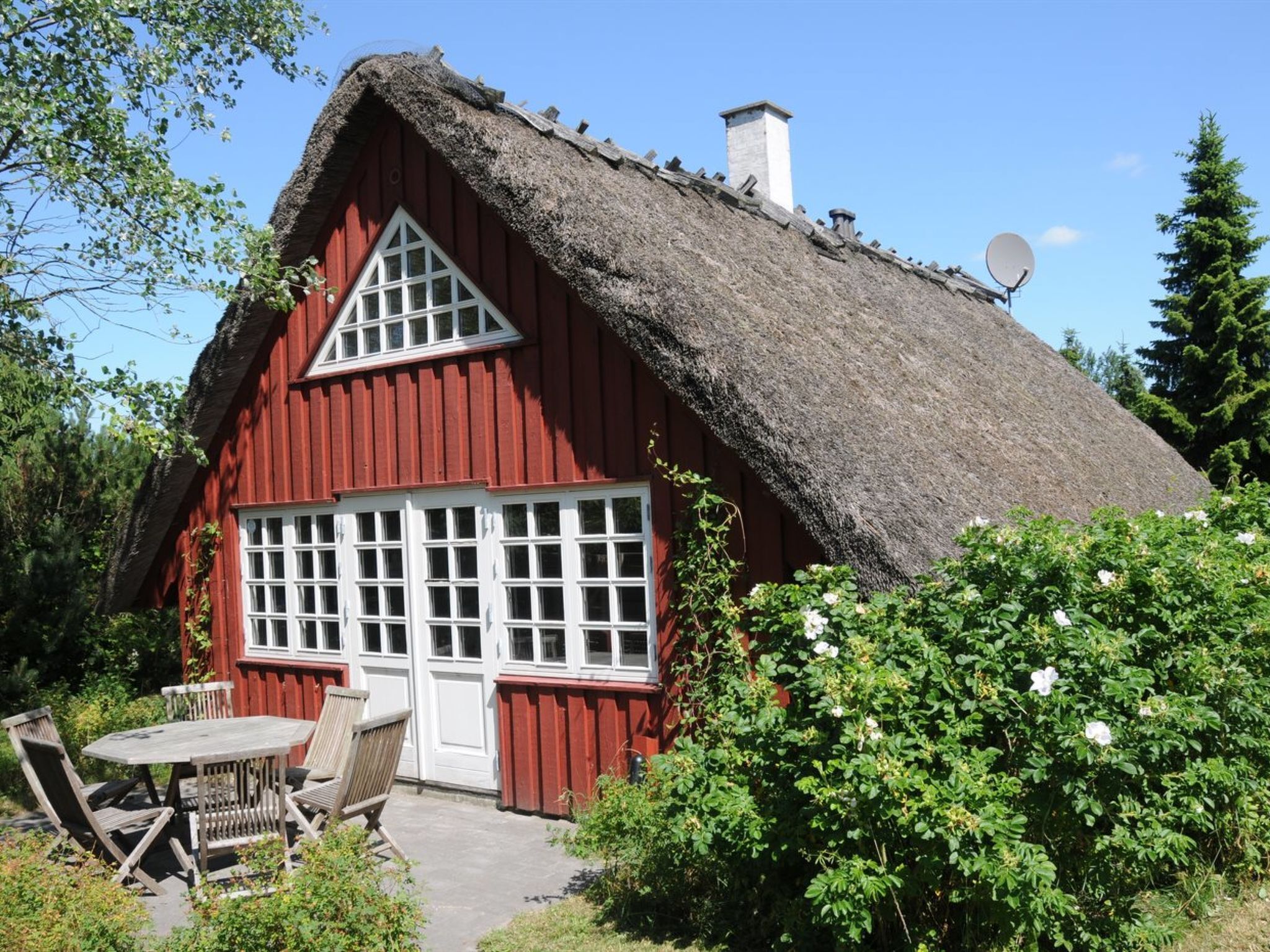 A red wooden house with a thatched roof, white windows, and a satellite dish.