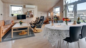 Ein modernes Wohnzimmer mit Holzboden, einem Fernseher, einer Couch, einem Esstisch mit Stühlen und einem großen Fenster mit Blick.