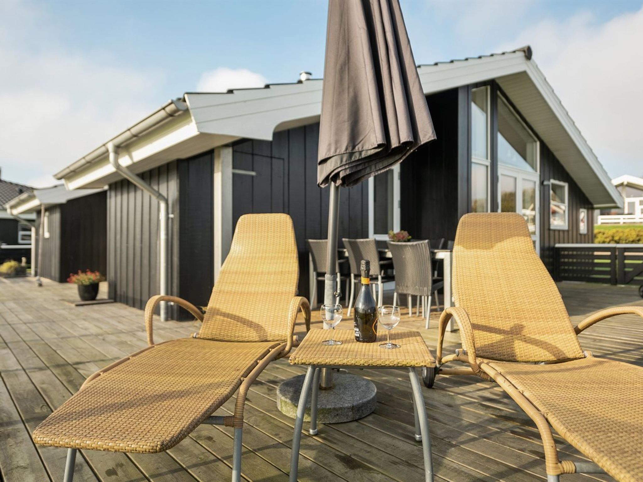 Eine Terrasse mit zwei Korlounge-Stühlen, einem Tisch mit Flasche und Gläsern sowie einem großen Sonnenschirm.