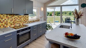 Eine moderne Küche mit grauen Schränken, einer gefliesten Spritzschutzleiste und einem großen Fenster mit Blick auf einen Garten.