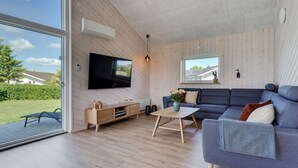 Ein modernes Wohnzimmer mit großem Fernseher, Holzwandverkleidung, einem grauen Sofa und einem Holztisch.
