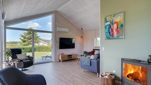 Ein modernes Wohnzimmer mit Kamin, Fernseher und einem großen Fenster mit Blick ins Freie.