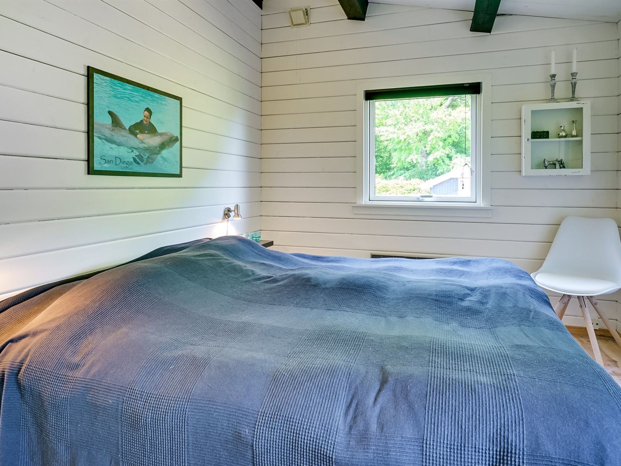 Une chambre à coucher avec un lit, une fenêtre, une chaise et un tableau encadré au mur.
