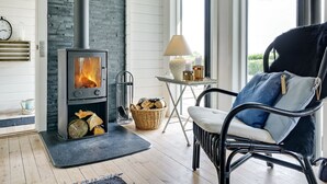A cozy room with a wood-burning stove, a wicker chair, and a small table with a lamp.