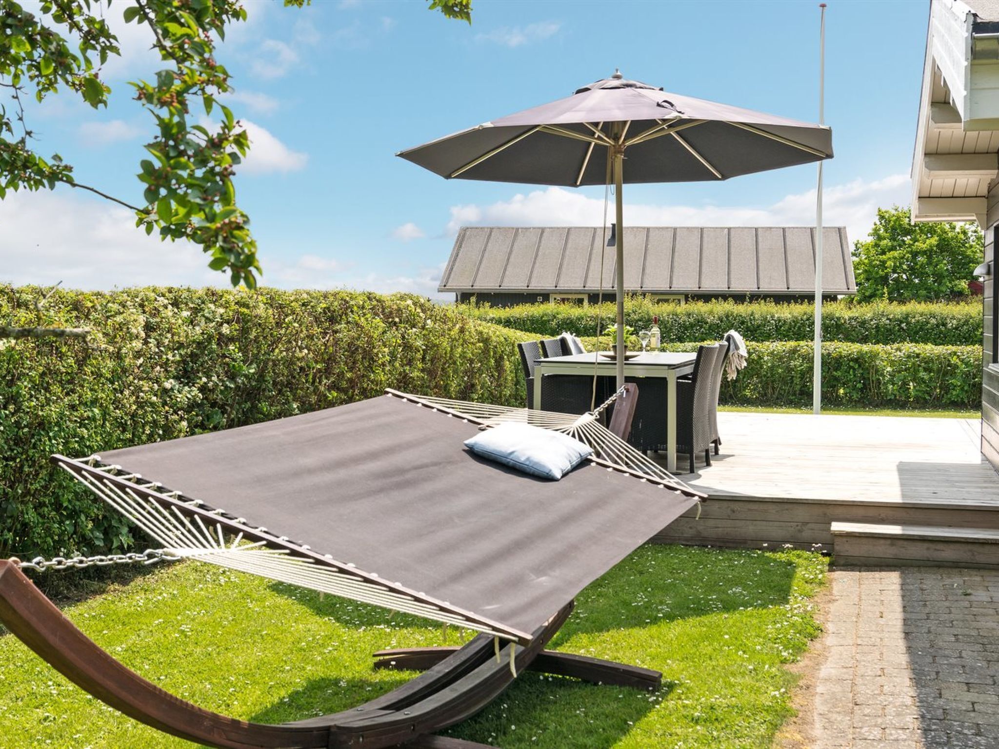 Un hamac avec un coussin, une table avec des chaises et un parasol dans un espace aménagé en jardin.