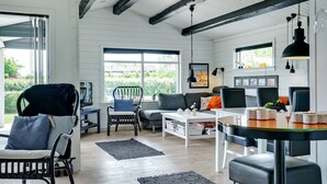 A spacious living room with a large window, a black chair, a grey sofa, and a dining area with a table and chairs.