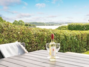 A table with a bottle of wine and a glass, set against a backdrop of a lush garden and a lake. - "Ølwir" - 400m to the fjord by Interhome (Egernsund)