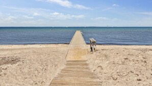Une jetée en bois qui mène à une plage de sable, avec l’océan en arrière-plan.