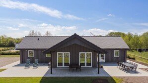 Un bâtiment moderne doté d’un toit en pente, de grandes fenêtres et d’un patio aménagé avec des sièges extérieurs.