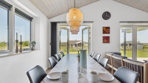 Un espace repas comprenant une longue table, des chaises et un luminaire suspendu.