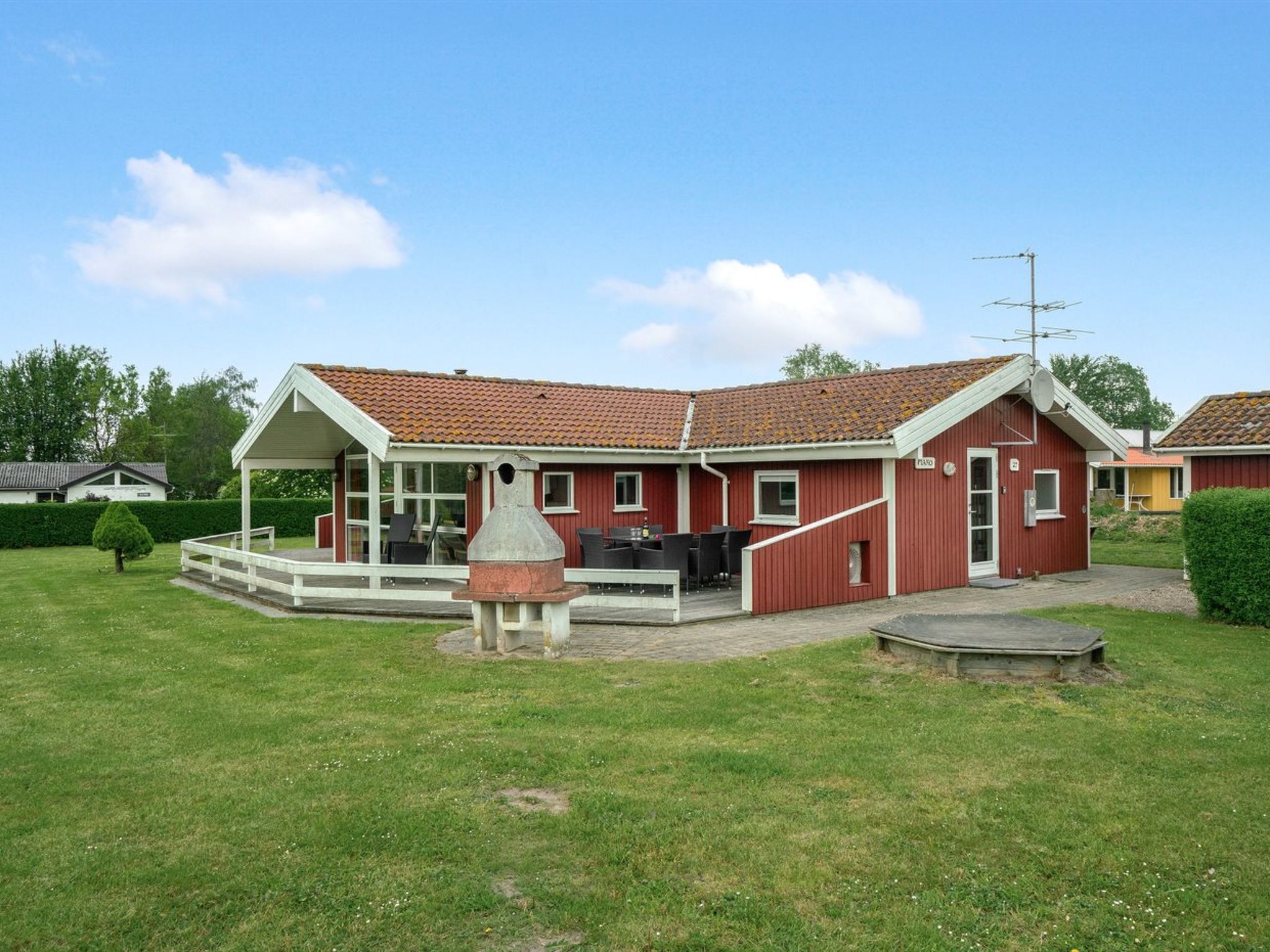 A red house with a covered patio and a barbecue grill in the front yard.
