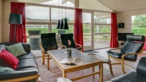 Een ruime woonkamer met een houten plafond, grote ramen en een schuifpui naar een buitenruimte.