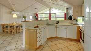 Een ruime keuken met een groot eiland, houten kastjes en een eethoek met een tafel en stoelen.