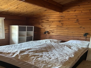 Une pièce aux murs lambrissés, avec un lit, une armoire blanche et une lampe de chevet.