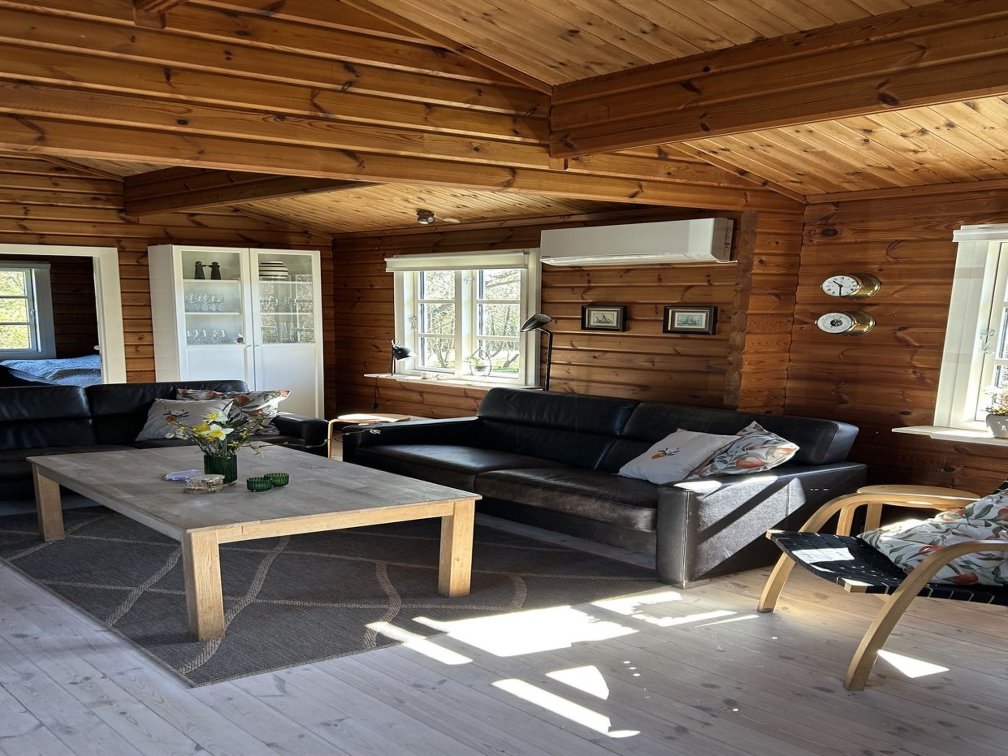 A cozy cabin interior with a wooden ceiling, a sofa, a coffee table, and a window with a view.