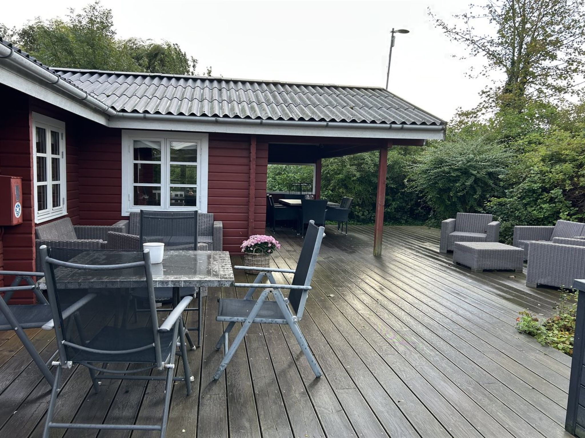 A covered outdoor area with a table and chairs, a small building with a red exterior, and a wooden deck.