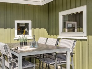 An outdoor patio with a table and chairs, two windows, and a green wall. - "Guldborg" - 400m to the fjord by Interhome (Egernsund)
