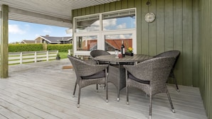 A covered outdoor patio with wicker furniture and a table, a large window, and a view of houses. - "Guldborg" - 400m to the fjord by Interhome (Egernsund)