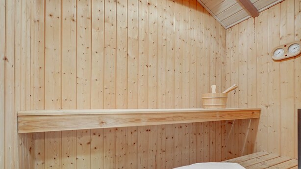 A wooden sauna room with a bench, a shelf, and a wooden container.