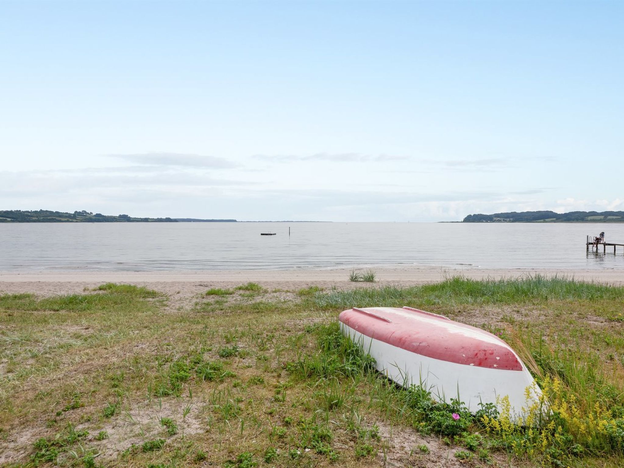 Uma praia com um barco na areia e outro barco ao longe no mar.