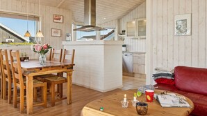 L’intérieur chaleureux d’un chalet avec une table à manger en bois, des chaises, un canapé rouge et une table basse agrémentée de bougies et de magazines.