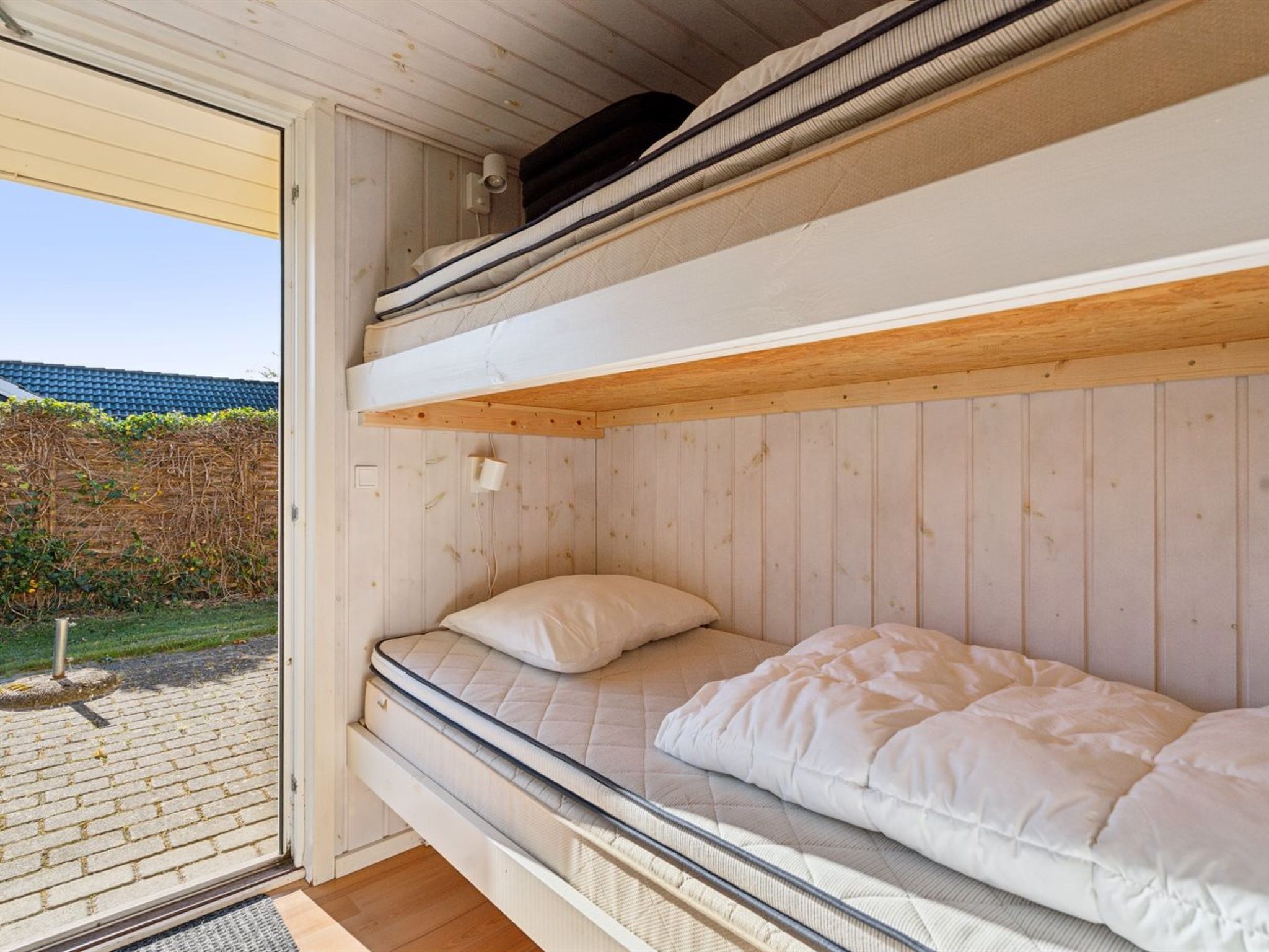 A bunk bed with a wooden headboard and a mattress with white bedding.