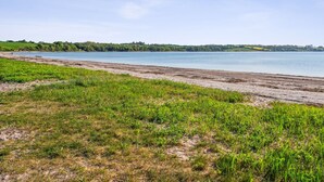 Une plage avec une étendue d’herbe au premier plan et un lac paisible en arrière-plan.