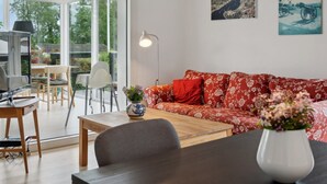 A modern living room with a red patterned sofa, a wooden coffee table, and a dining area with a TV and chairs.