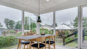 A dining area with a table and chairs, large windows, and a view of the outdoors.