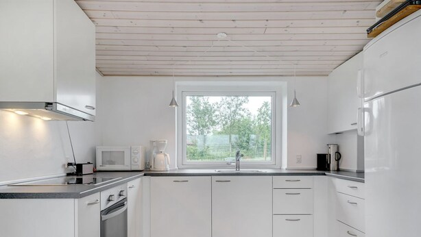 A modern kitchen with white cabinets, a built-in oven, a microwave, a coffee maker, and a window providing a view of greenery outside.