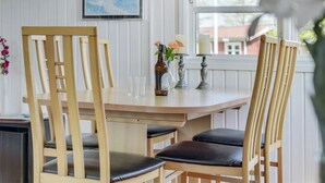A dining area with a wooden table, two chairs with leather cushions, a hanging light fixture, and a vase with flowers.