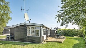 A single-story house with a satellite dish, a deck, and a lawn.