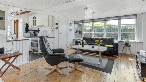 A spacious living area with a wooden floor, a black leather sofa, a coffee table, and a kitchen in the background.