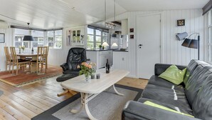 A cozy living room with a black leather sofa, a wooden dining table with chairs, and a kitchen area with white cabinets and a microwave.