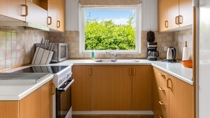 Eine kleine Küche mit Holzausstattung, einem Einbauofen, einer Mikrowelle, einer Kaffeemaschine und einem Fenster mit Blick auf Grünflächen.