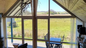 A room with large windows offering a view of a grassy field. There is a table and chairs outside the windows. - "Sigbritt" - 100m from the sea by Interhome (Broager)