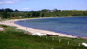 A coastal beach scene with a sandy shore, a few boats, and a grassy area with a fence. - "Sigbritt" - 100m from the sea by Interhome (Broager)