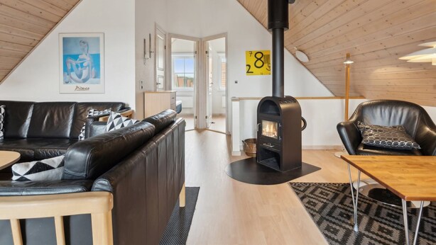 Un acogedor salón tipo loft con un sofá de cuero negro, una mesa de comedor de madera y un estufa de leña negra.