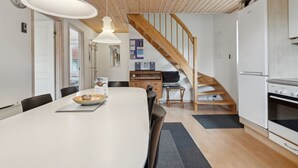 Una cocina moderna con una escalera de madera, un comedor con una mesa blanca y un refrigerador.