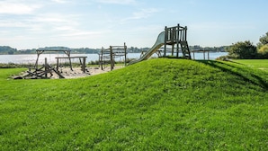 Une aire de jeux avec un toboggan et des structures d’escalade, située près d’un lac.