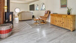 Ein gemütliches Wohnzimmer mit Kamin, einer Couch, einem Ledersessel, einem Holzschrank und einem großen Fenster.