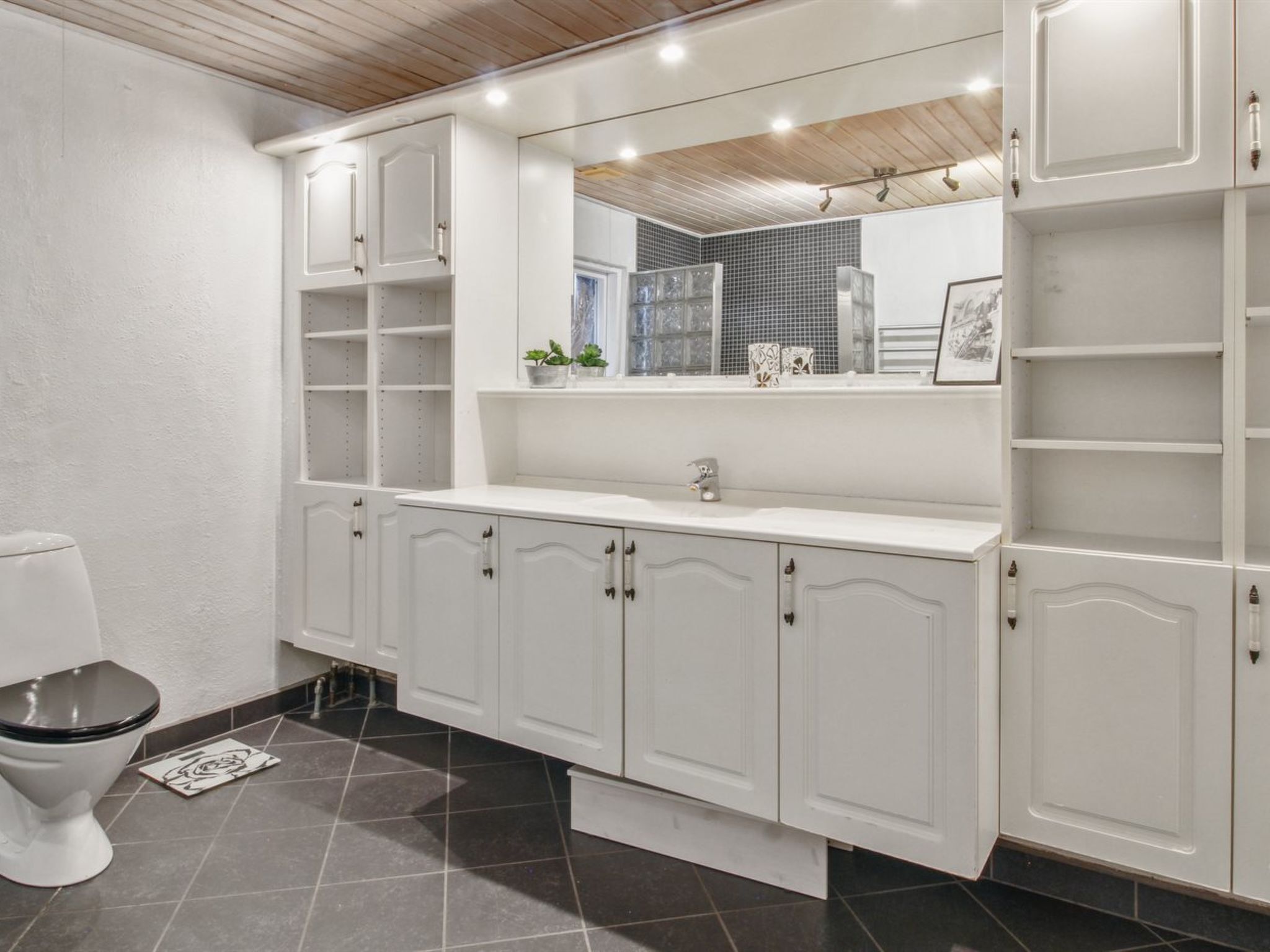 A modern bathroom with white cabinetry, a large mirror, and a toilet.