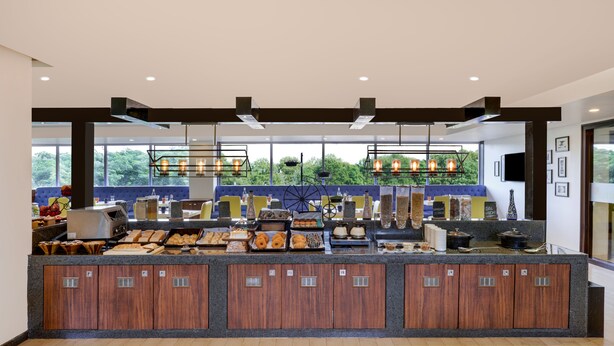 A buffet area with a variety of food items, a large window with a view of greenery, and a modern design with wooden cabinets and pendant lighting. - Lemon Tree Hotel Hubli (Hubli)