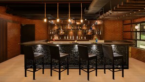 A bar area with a brick wall, a bar counter, and multiple bottles. There are four chairs around the bar. - Lemon Tree Hotel Hubli (Hubli)