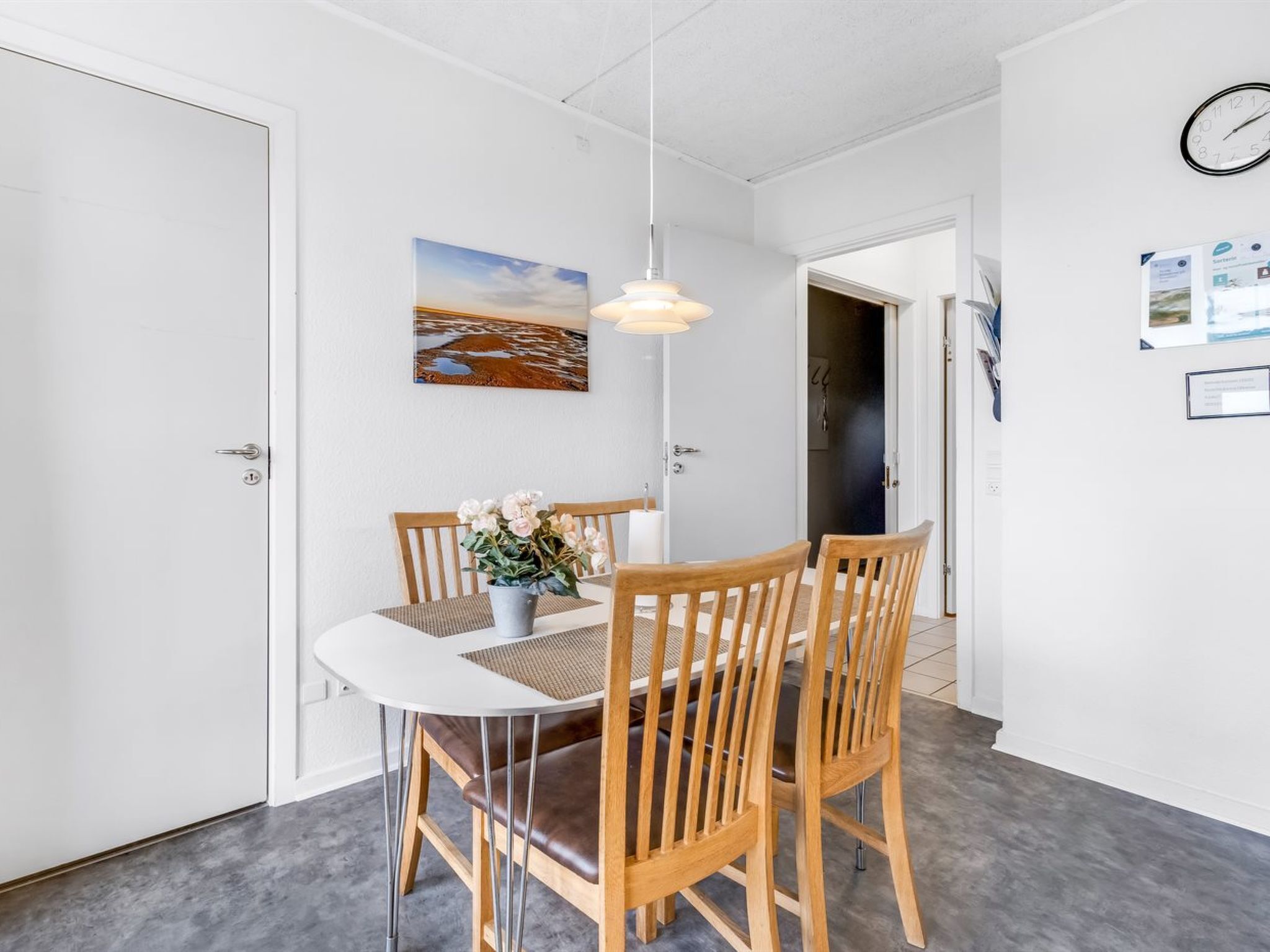 Et spiseområde med et rundt bord, træstole, en hængende lysekrone og et maleri på væggen.