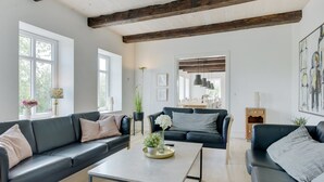 Un salón moderno con dos sofás de cuero negro, una mesa de centro de color claro y un área de comedor visible a través de una puerta abierta.