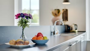 Una cocina moderna con una isla grande, un jarrón de flores, un cuenco de fruta y un plato de pasteles.