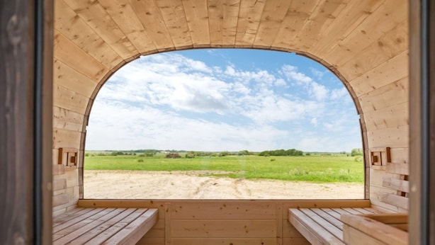 Una cabaña de madera con un amplio ventanal de arco que ofrece vistas a un campo verde y un cielo despejado.