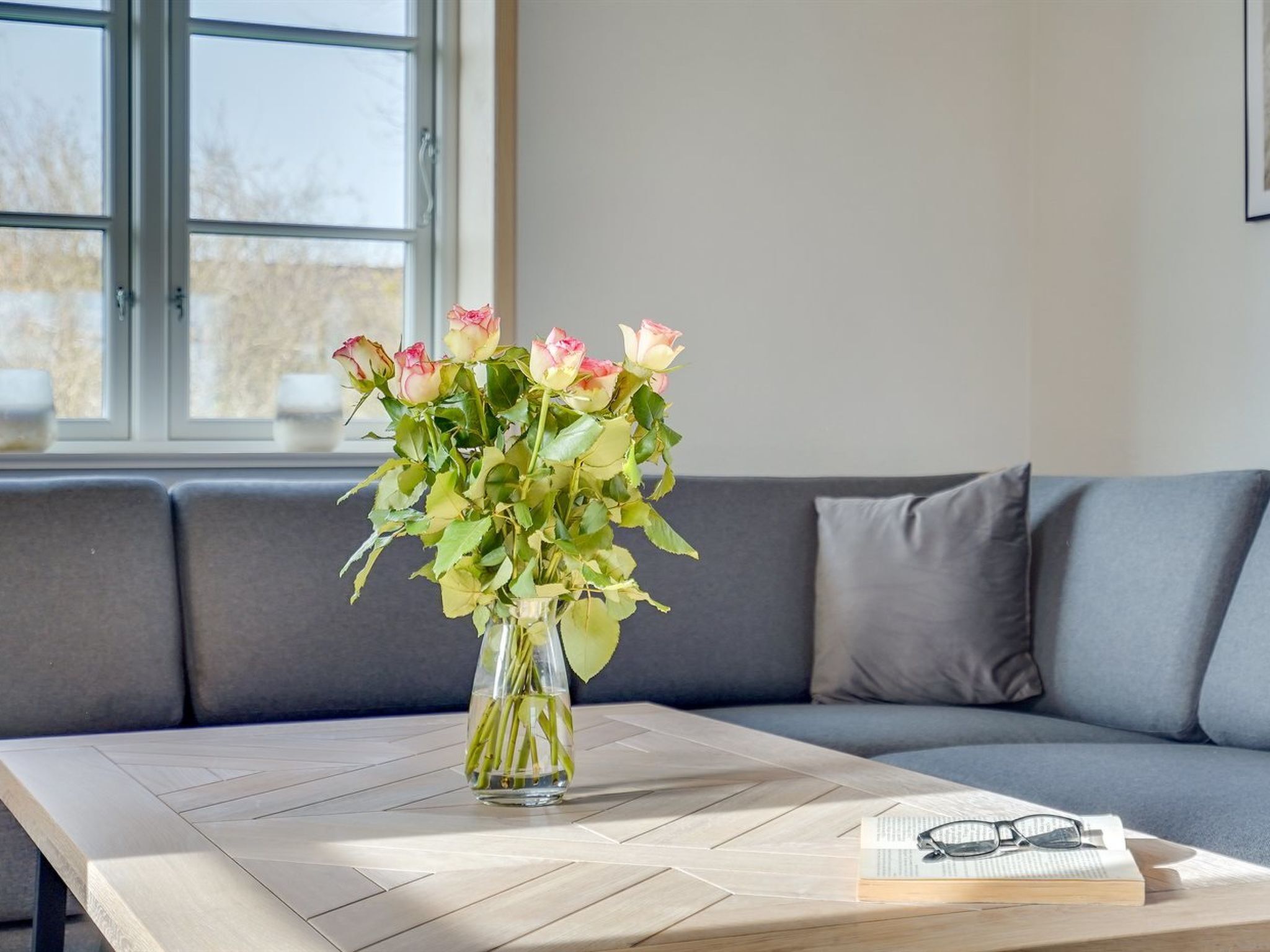 A room with a grey sofa, a wooden coffee table, and a vase with flowers.
